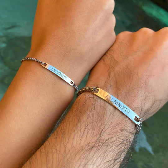 Couple wearing matching silver engraved bracelets, both steel bars engraved with the same date in Roman numerals